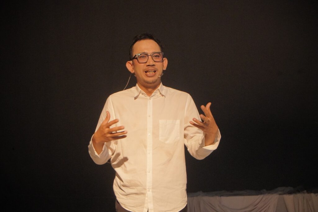 Whatsapp image 20260609 at 16 47 11 catrawarta Man in a white shirt with a headset microphone speaking on a dark stage gesturing with his hands